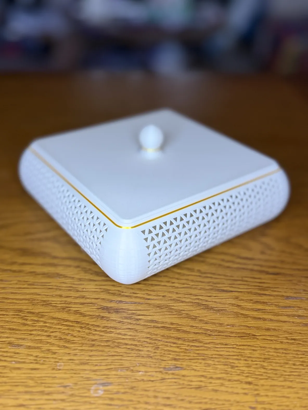 Vide-poche blanc fermé vu de trois quarts, filet doré entre la base et le couvercle, bouton sphérique blanc